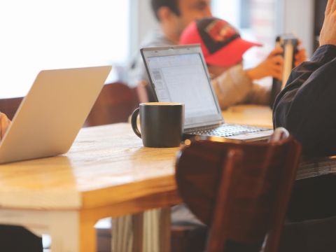 Menschen sitzen an Tisch und arbeiten an Laptop