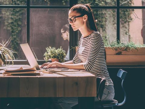 Junge Frau arbeitet an Laptop - Auch bei mobiler Arbeit auf Ergonomie am Arbeitsplatz achten