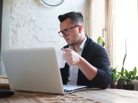 Mann mit Kaffeetasse sitzt vor Laptop