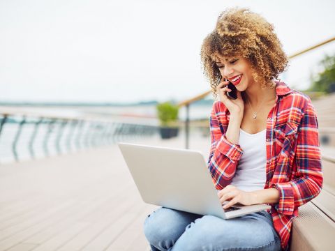 Glücklich lächelnde Frau telefoniert und hat einen Laptop auf ihrem Schoß