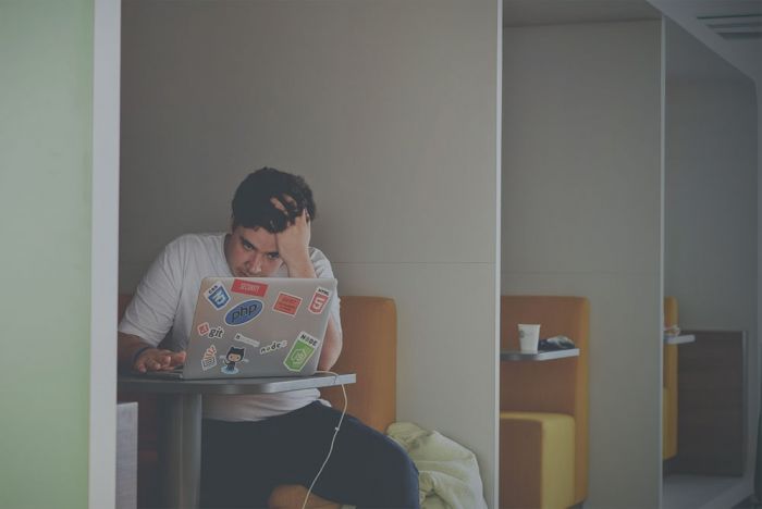 A young man seat desperately in front of his laptop because there is no room booking systems to book a room for concentrate work.